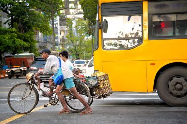 China Town, Yangon - 21 Ekim 2017: Bir üç tekerlekli bisiklet taksi şoförü dikkatle bir sepet muz ve meşgul bir kavşak ile bir yolcu dolu dolu onun üç tekerlekli bisiklet iter.