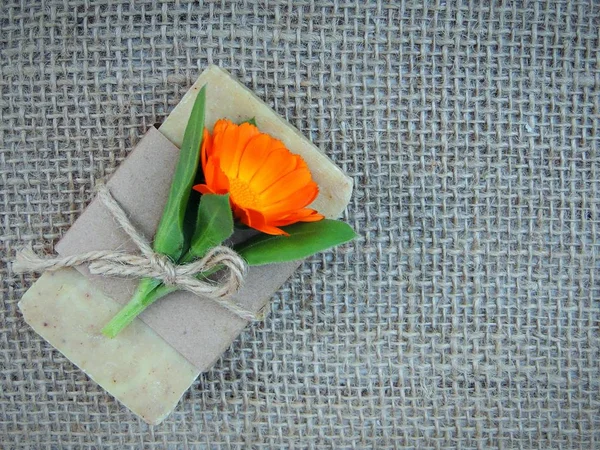 Çuval bezi zemin üzerine calendula çiçek olan el yapımı doğal sabun çubuk.