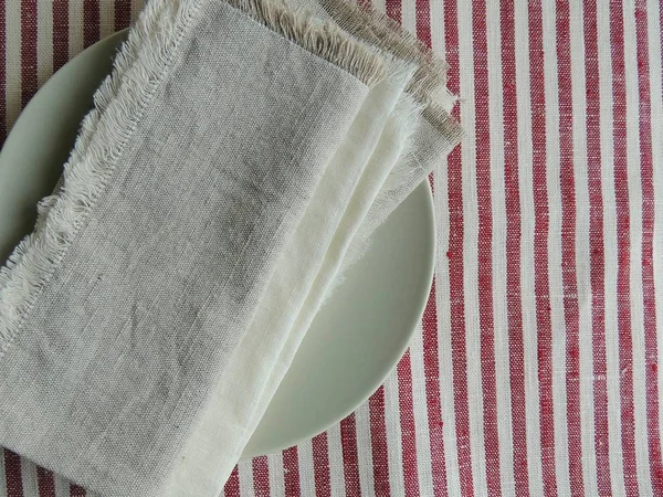 Plate, linen towels, handmade white linen no sew napkin on striped white linen tablecloth. Top view.