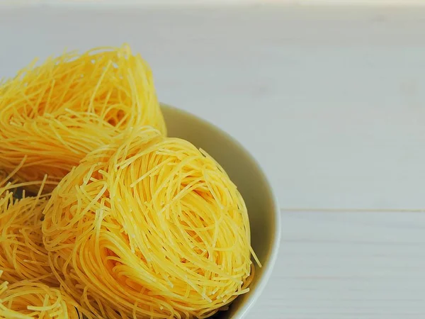 Raw pasta, macaroni nests in a bowl on white wooden background. Pasta italian food cooking.