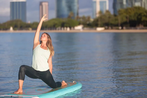 Hübsche Frau im modifizierten Krieger macht Sup Yoga auf dem Wasser — Stockfoto