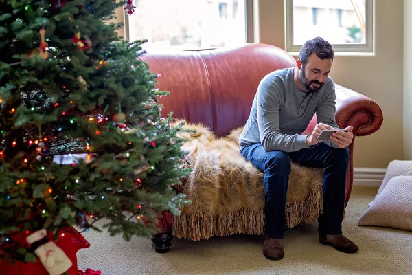Man met behulp van smart phone tijdens Kerstmis thuis Stockafbeelding