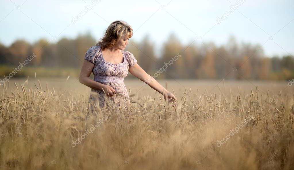 lonely beauty mature woman, walks on the wheat field, horizontal photo
