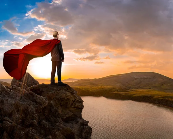 ある実業家が頂上に立ち赤いレインコートが風になびいています コンセプト達成 — ストック写真