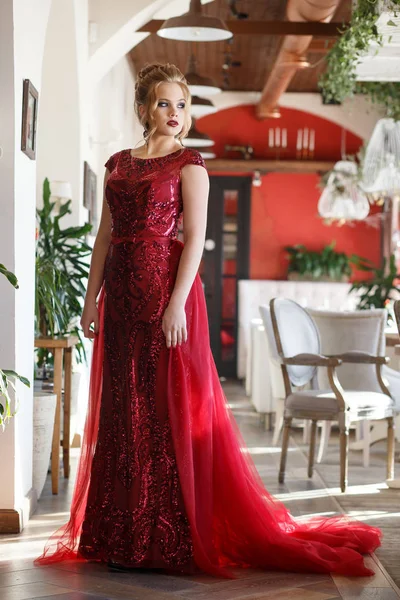 Hermosa mujer posando en vestido largo rojo con tren en el interior del restaurante de lujo —  Fotos de Stock