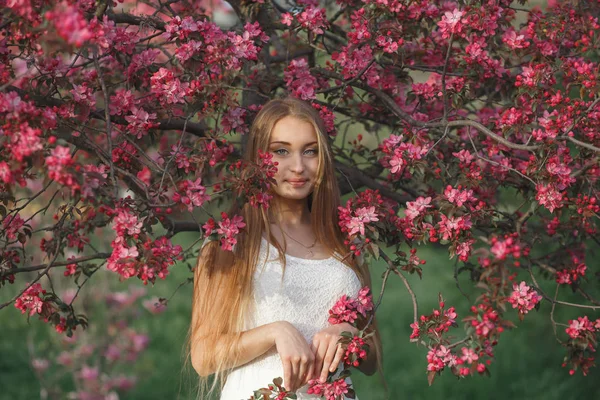 Young blonde woman standing in a blooming garden. Blooming cherry. Portrait of beautiful woman. Close up of woman face. Sakura blooming, spring evening time — Stock Photo, Image