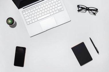 Modern beyaz öğrenciler Resepsiyon Masa laptop, boş ekran akıllı telefon, şık gözlük, siyah defter ve kalem. Kopya alanı ile Üstten Görünüm.