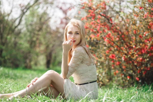 Glückliche blonde Frau im Frühling sitzt in einem blühenden Garten und genießt die Natur — Stockfoto