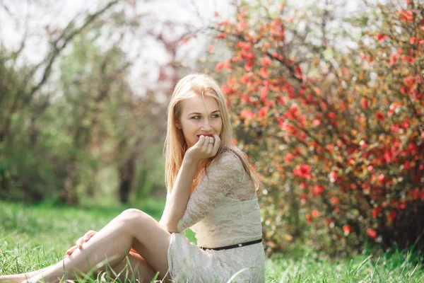 Glückliche blonde Frau im Frühling sitzt in einem blühenden Garten und genießt die Natur — Stockfoto