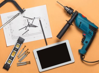 İnşaat araçları onarım ve turuncu-kahverengi masa üzerinde beyaz tablet set: Matkap, çekiç, çizim, pense, kendi kendine vidalar, rulet, düzey, dokunarak kalem. Üstten Görünüm