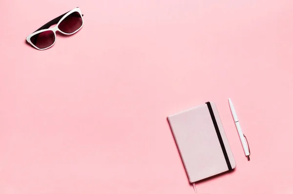 Diario rosa, bolígrafo blanco, gafas sobre fondo de texto. plano, vista superior. Espacio de trabajo femenino — Foto de Stock