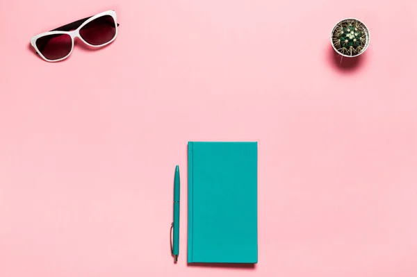 Creativo plano laico foto de escritorio del espacio de trabajo con cuaderno de aguamarina, gafas, cactus copia espacio fondo rosa, estilo minimalista — Foto de Stock