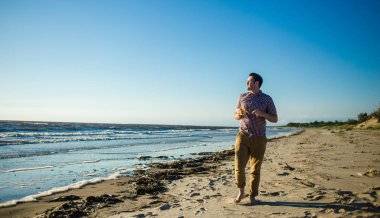 Rahat hafif giysiler giyen narenciye suyu ile okyanus önünde gülümseyen mutlu yakışıklı adam