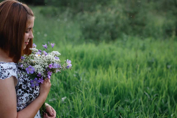 Красива молода жінка з бугаєм лугових квітів насолоджується польовими ароматами . — стокове фото