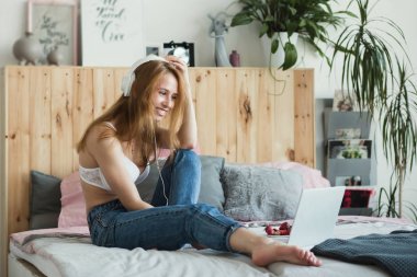 Genç seksi sarışın kadın laptop yatak yatak odasında otururken, online flört