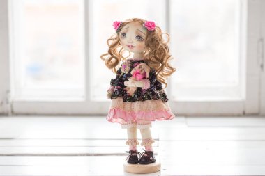 Hafif pembe ve mavi ve yeşil gözlü, uzun kahverengi kıvırcık saçlı Tekstil el yapımı antika oyuncak bebek portresi beyaz arka plan üzerinde içinde nazik baskı ile elbise. Küçük Tekstil oyuncak ayı elinde