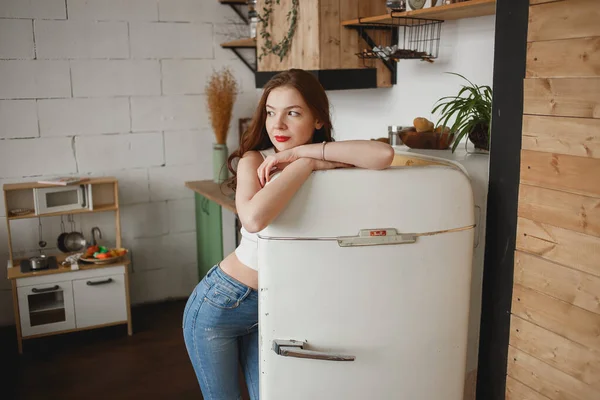 Slender girl in jeans opening retro fridge door and looking into window — Stock Photo, Image