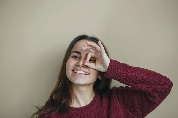 Gelukkige jonge vrouw tonen ok symbool en vriendelijk op zoek naar camera op beige muur. Ze droeg een bordeaux trui. Vriendelijke blik — Stockfoto