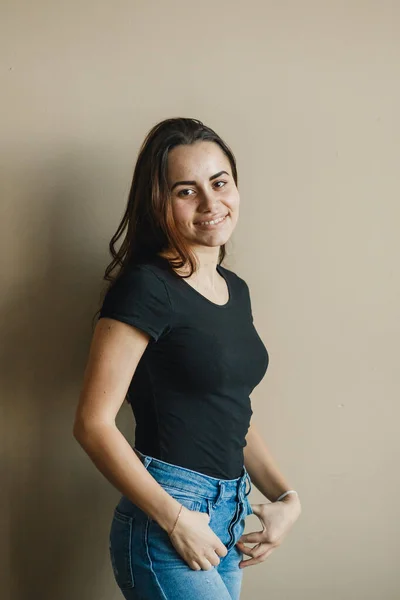 Jovem feliz amigável olhando para câmera no fundo bege. Ela vestiu-se de t-shirt preta e jeans azul — Fotografia de Stock