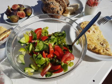 Balkonda sağlıklı bir kahvaltı. Kabak çekirdeği ve peynirli tam tahıllı ekmek. Salatalık ve domatesli salata. Taze incir. Yoğurtlu çilek. Doğrudan güneş ışığının üzerinde