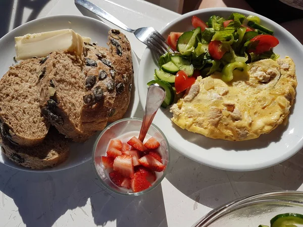 Desayuno saludable en el balcón. Pan integral con semillas de calabaza y queso. Ensalada de pepinos frescos y tomates. Higos frescos. Fresas con yogur. Por encima de la luz solar directa — Foto de Stock