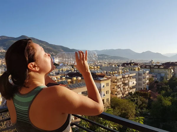 Young sports woman drinking fresh water from the bottle in the sunny balcony refreshing herself — Stock Photo, Image