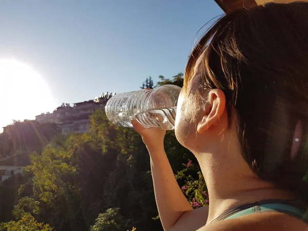 Young sports woman drinking fresh water from the bottle in the sunny balcony refreshing herself — Stock Photo, Image