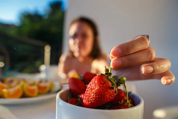 Chica toma fresas de una taza en el balcón soleado — Foto de Stock