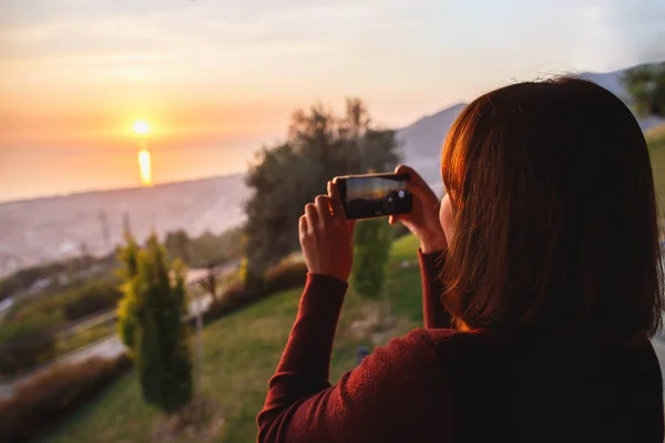 Voyageur femme utiliser téléphone mobile prendre une photo de belle de la nature coucher de soleil au sommet de la vue sur la mer de montagne . — Photo