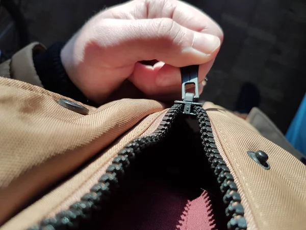 The mans hand zips zip up on the jacket. Zipper close up in hard light