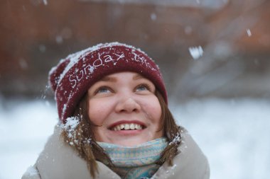 İnsanlar, mevsim ve bayram konsepti. Kış parkında gülümseyen genç bir kadının portresi. Kırmızı kış şapkası ve kırmızı eldivenler giydi. Karlı hava