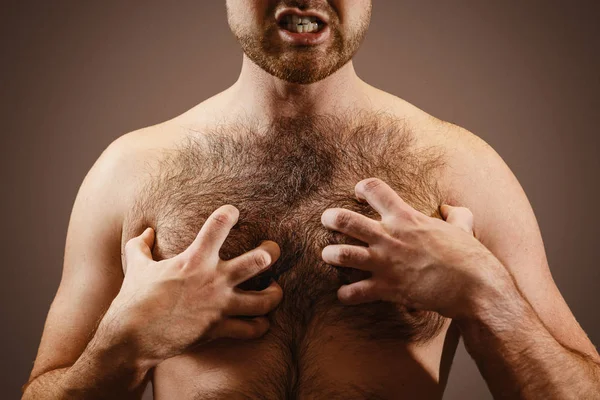 Male concept of testosterone. A man holds his hairy chest close-up