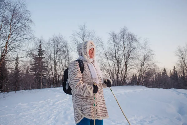 Ormanda kış günbatımını bekleyen mutlu yaşlı kadın. İskandinav yürüyüşü — Stok fotoğraf