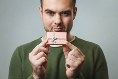 Genç ve şık bir adam güzel pembe bir kutu tutuyor. Sevgililer Günü hediyesi gri bir duvarın arkasında.