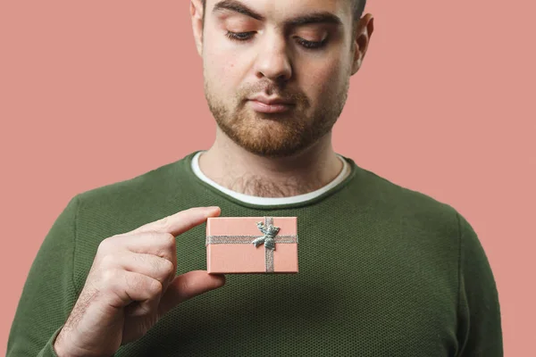 A young stylish man holds a beautiful pink box with a gift for Valentines Day against the backdrop of a pink wall — стокове фото