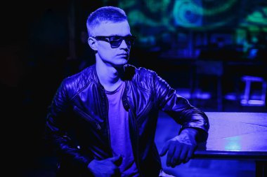 Deri ceketli, güneş gözlüklü ve neon ışıklı yakışıklı bir adam.