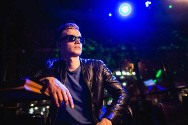 Deri ceketli, güneş gözlüklü ve neon ışıklı yakışıklı bir adam.