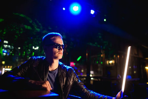 Homem bonito em jaqueta de couro com óculos de sol testando luz LED em luzes de néon da boate — Fotografia de Stock