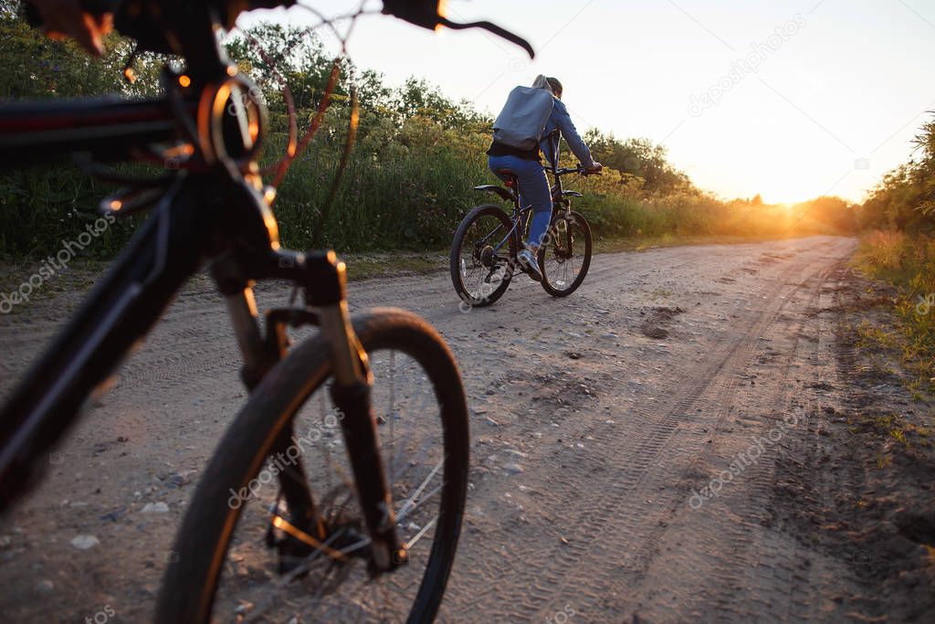 A woman rides her bike on a field road at sunset