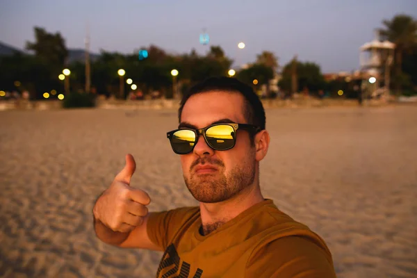 Hombre atractivo en gafas amarillas se relaja en la playa al atardecer —  Fotos de Stock