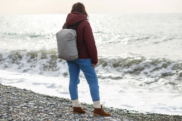 Eine Frau in Jacke und Rucksack beobachtet die Meereswellen von hinten — Stockfoto