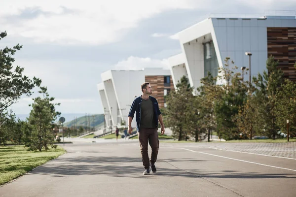Handsome brutal man walks next to modern university buildings