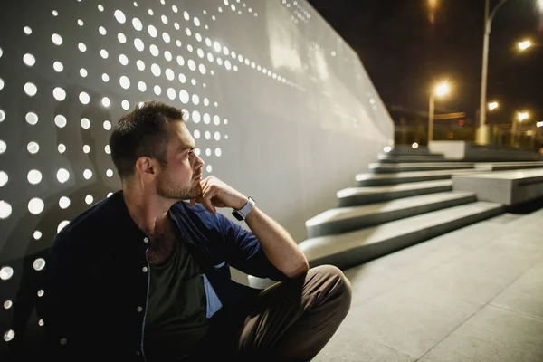 Чоловік сидить і думає на сучасній нічній набережній у світлі ліхтарів — стокове фото