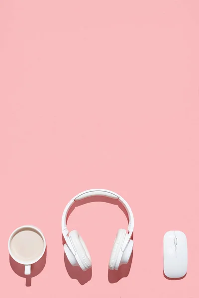 Trendy flat lay mockup with wireless headphones, wireless mouse and cup of cocoa on pink colored table. Directly above. Modern feminine workspace. — Stock Photo, Image