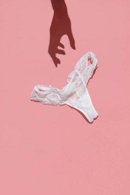 Kadınların elleri pembe arka plandaki beyaz dantel külotlara uzanır.