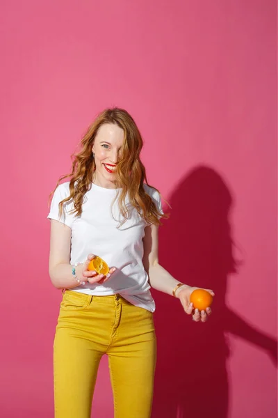 Oranje fruit, gezond eten, echte emoties - een jonge blonde vrouw jongleren sinaasappels op roze achtergrond — Stockfoto