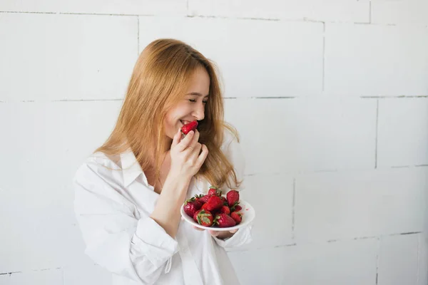 Jovem mulher magra sexy comendo delicioso morango no fundo branco. Luz natural, espaço de cópia — Fotografia de Stock