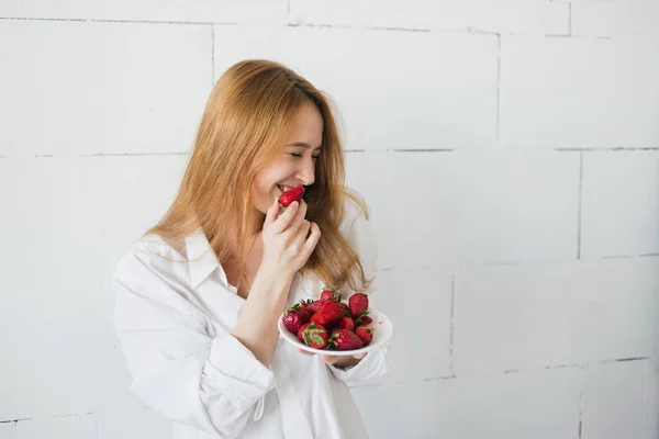 Giovane donna sottile sexy mangiare deliziosa fragola su sfondo bianco. Luce naturale, spazio di copia — Foto Stock