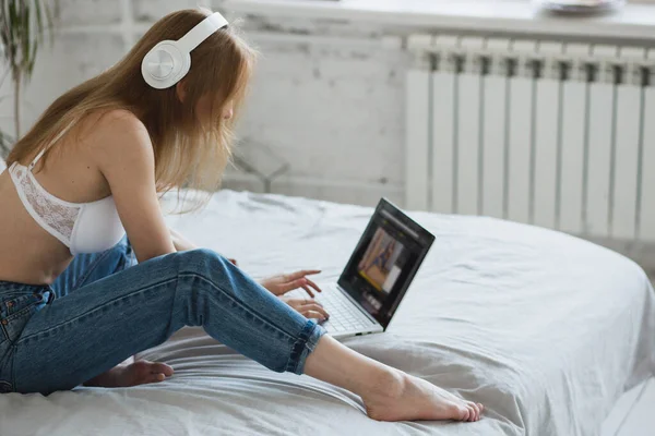 Молодая сексуальная блондинка флиртует онлайн на ноутбуке, сидит на кровати в спальне — стоковое фото