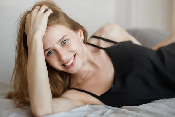 Fiatal érzéki szőke nő fekete szexi ruha fekszik a kanapén, és élvezi a pillanatot — Stock Fotó